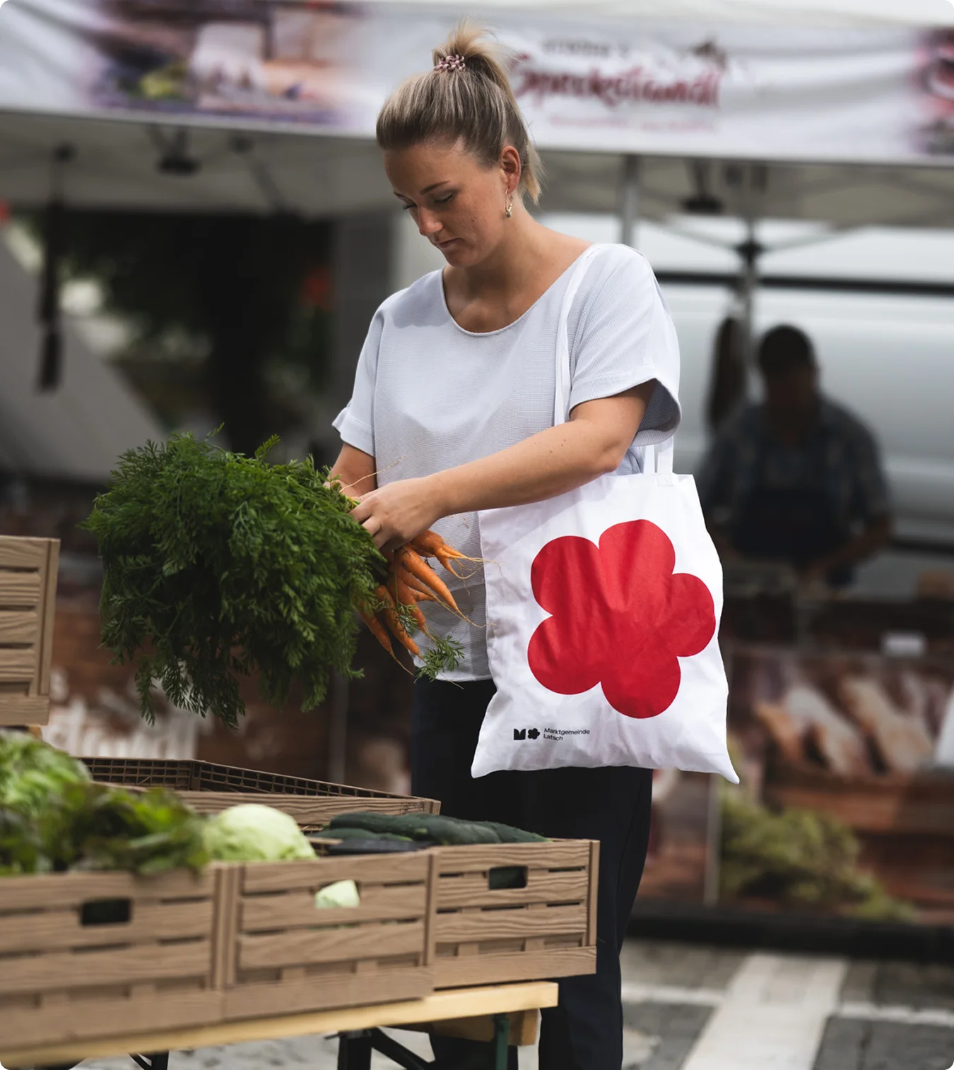 Frau mit Karottenbund und Jutebeutel am Wochenmarkt