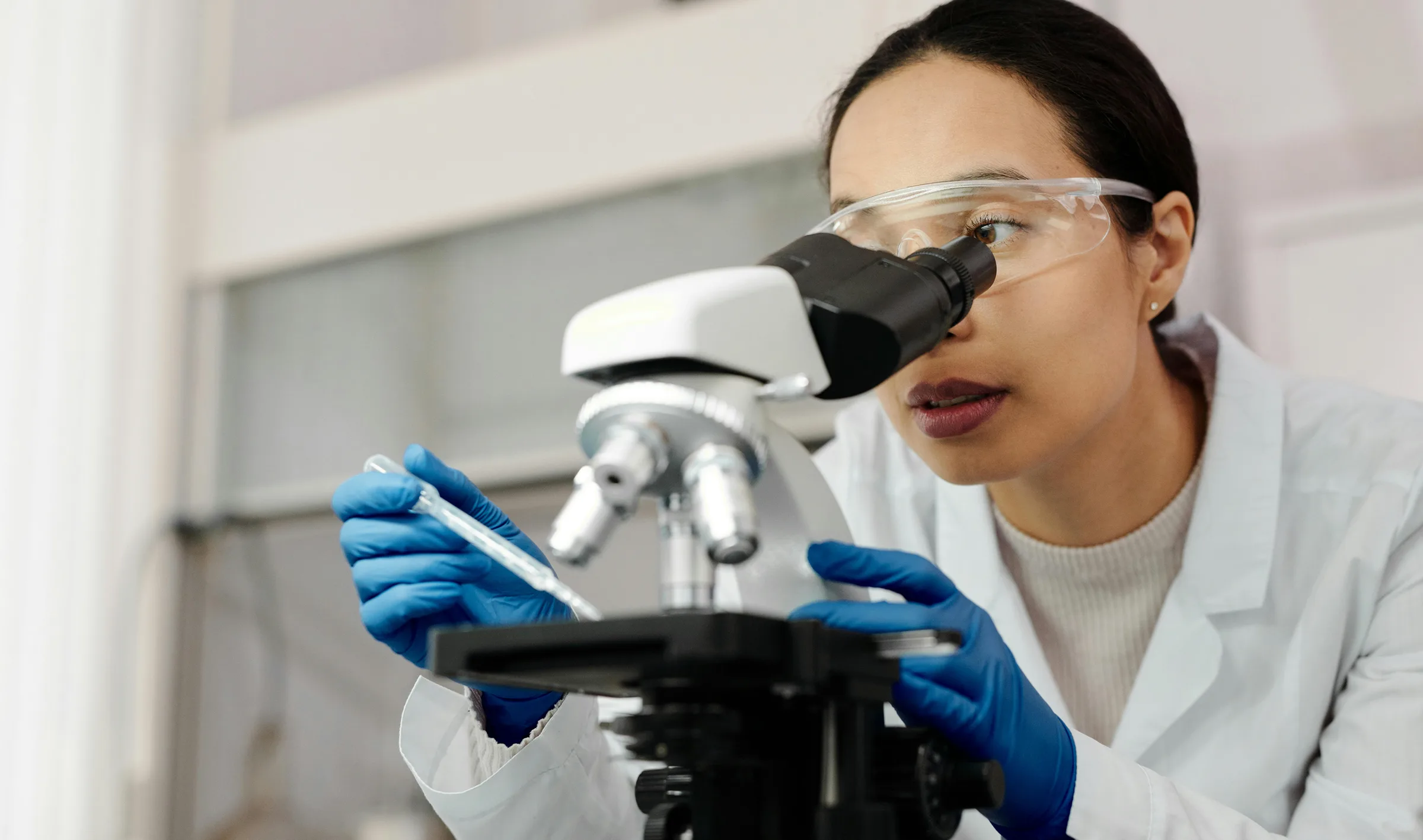 Laborantin mit Schutzbrille am Mikroskop