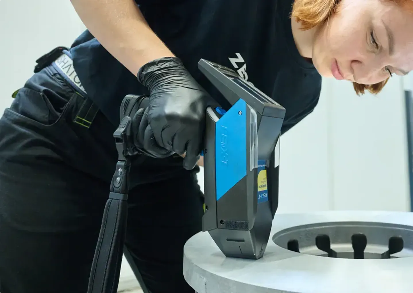 ZEROS-Mitarbeiterin prüft ein Metall-Bauteil mit dem RFA-Analysegerät